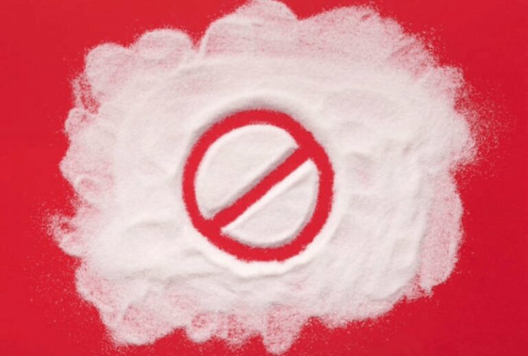 Hvidt sukker formet omkring et forbudsskilt på rød baggrund – symbol på sukkerstop.